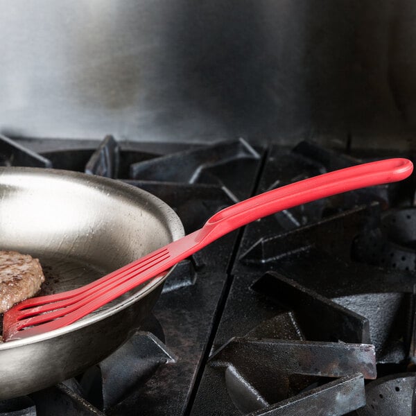 A red Mercer Culinary Hell's Tools slotted spatula in a pan of food.