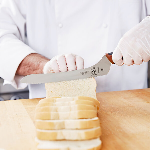 A person's hand using a Mercer Culinary brown handled serrated knife to cut bread.