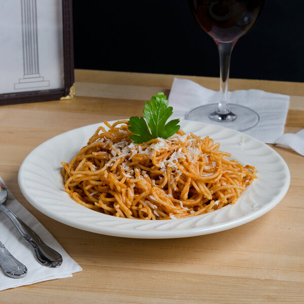 A Tuxton Meridian china bowl filled with spaghetti and a glass of wine on a table.