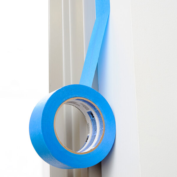 A roll of 3M ScotchBlue™ blue painter's tape on a white wall.