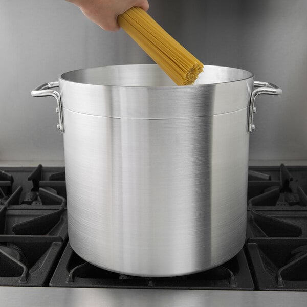 A hand holding yellow spaghetti over a silver stock pot.