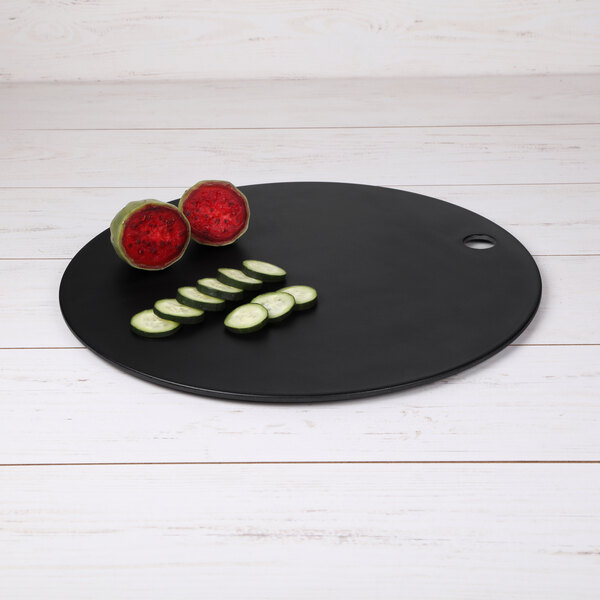 An Elite Global Solutions black round melamine and bamboo serving board with a sliced cucumber and watermelon on it.