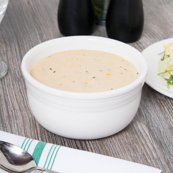 A Fiesta white china bowl filled with soup on a wood table.