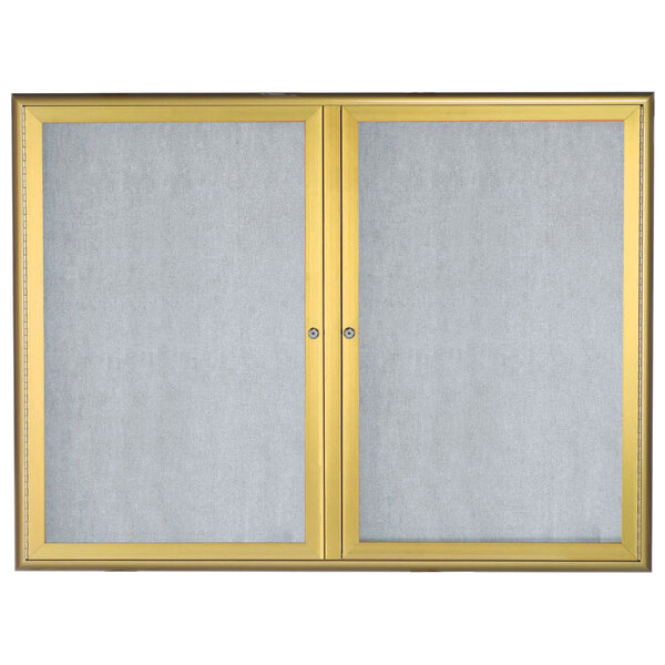 An Aarco enclosed bulletin board with gold frame and glass doors.