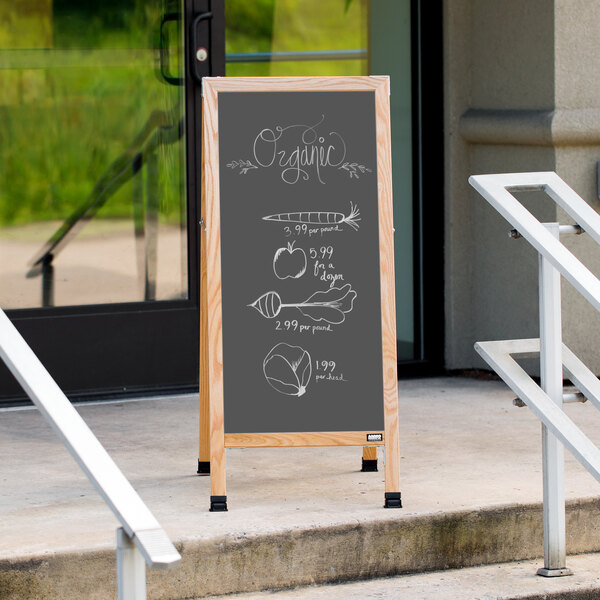 An Aarco oak A-frame chalkboard sign with slate gray writing displaying vegetables.