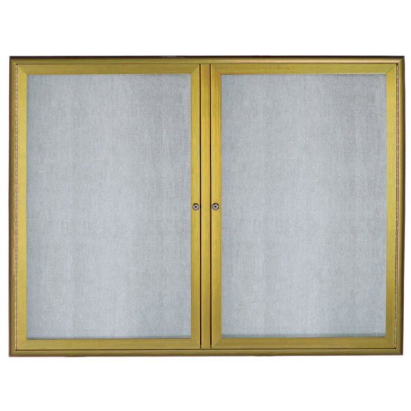 An Aarco white rectangular bulletin board with an antique brass frame and glass doors.