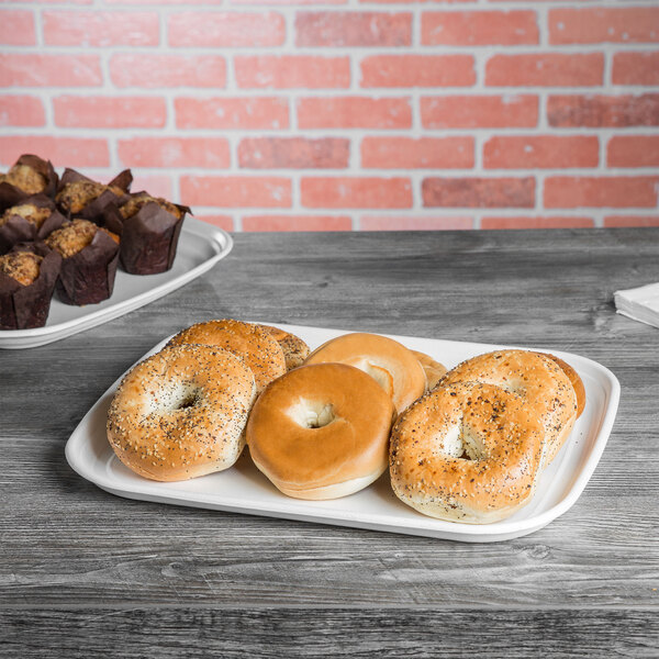 A white compostable sugarcane tray holding bagels and muffins on a table.