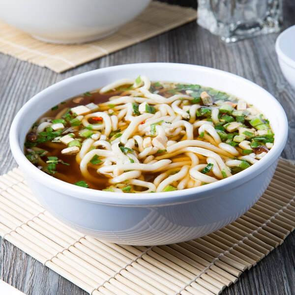 A bowl of soup with noodles, green onions, and chopsticks in a white Thunder Group melamine bowl.