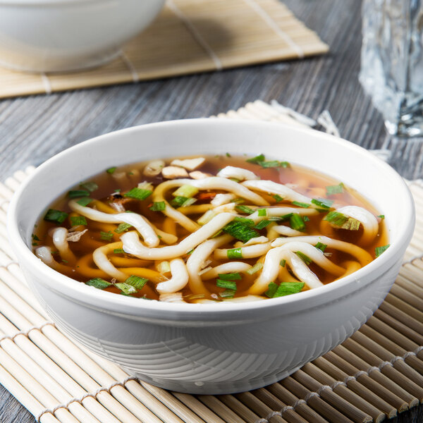 A bowl of soup with noodles and green onions served in a white Thunder Group melamine bowl.