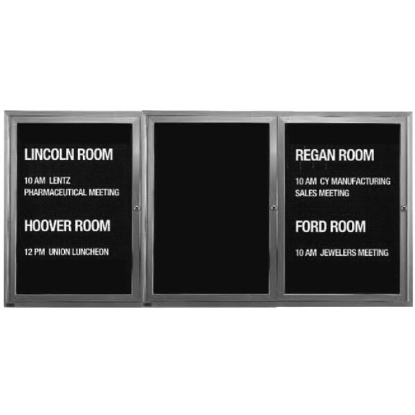 A black Aarco indoor message center with white text on three metal doors.