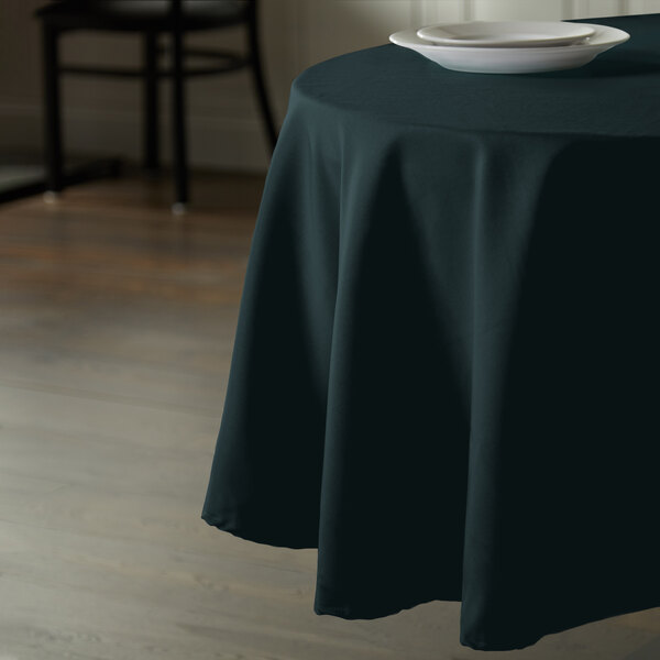 A hunter green Intedge round cloth table cover on a table with a plate on it.