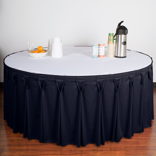A table with a navy Snap Drape table skirt on a white tablecloth with a bowl of oranges and a thermos.
