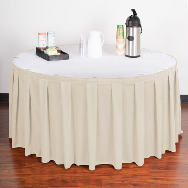A table with a Snap Drape box pleat table skirt in bone on it with a tray of drinks.