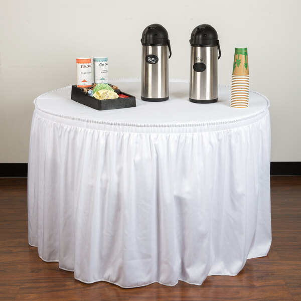 A table with a white Snap Drape table skirt, food containers, and a tray of food.