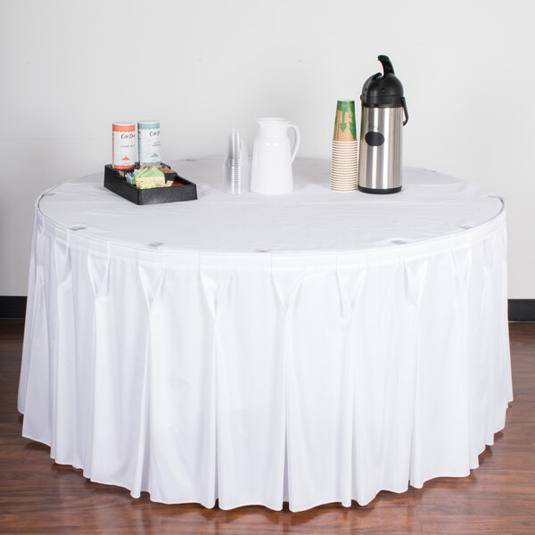 A table with a white tablecloth and Snap Drape white bow tie pleat table skirting with Velcro clips.