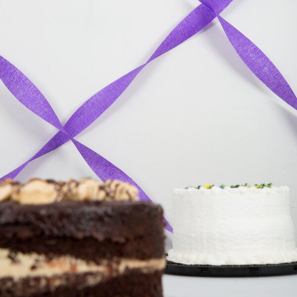 A chocolate cake with white frosting and a purple streamer.
