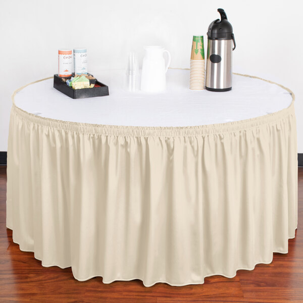 A table with a Snap Drape bone shirred pleat table skirt on a table with a tray of coffee cups.