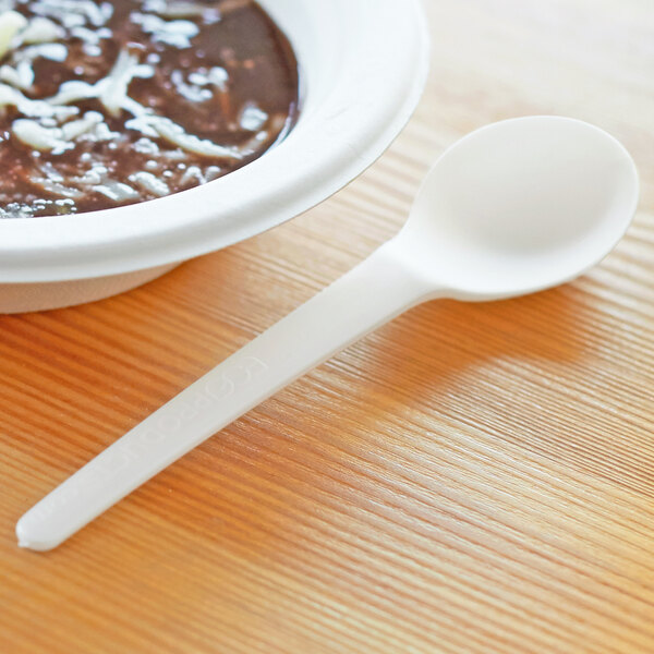 A bowl of soup with a white compostable plastic spoon on a table.