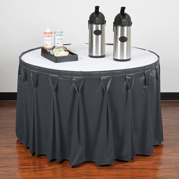 A table with a slate blue Snap Drape Wyndham table skirt with two bottles and a tray on it.