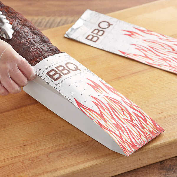 A hand using a knife to cut BBQ in a foil bag.