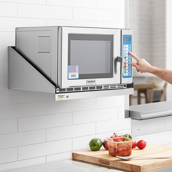 A person using a Regency stainless steel microwave shelf to heat food in a microwave.