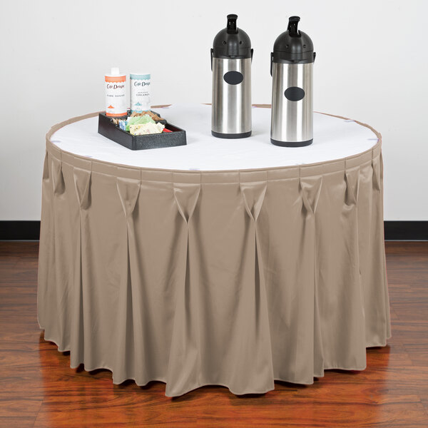 A table with a beige Snap Drape table skirt on it with a tray of food and two bottles.
