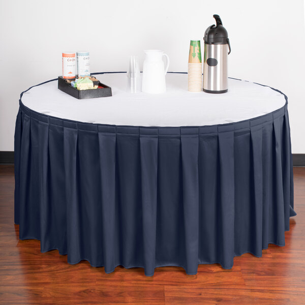 A table with a navy blue box pleat table skirt with Velcro clips on a white tablecloth and a tray of drinks.