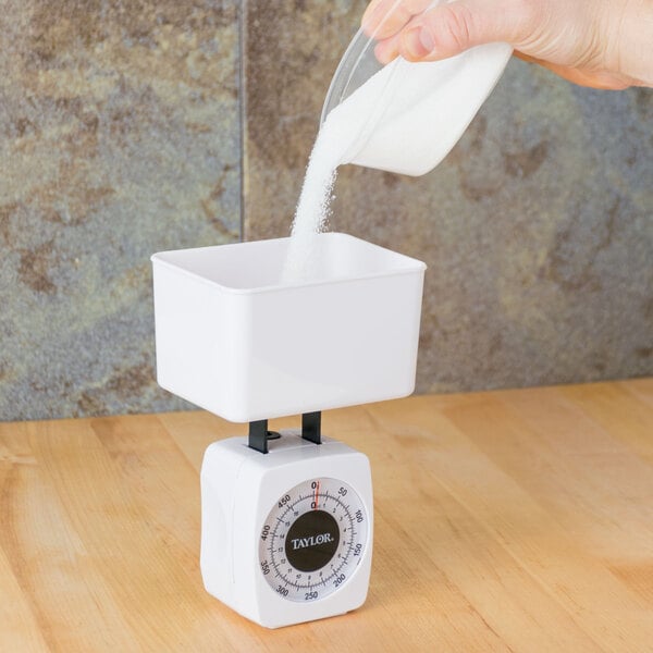 A person using a Taylor light duty portion scale to pour sugar into a container.