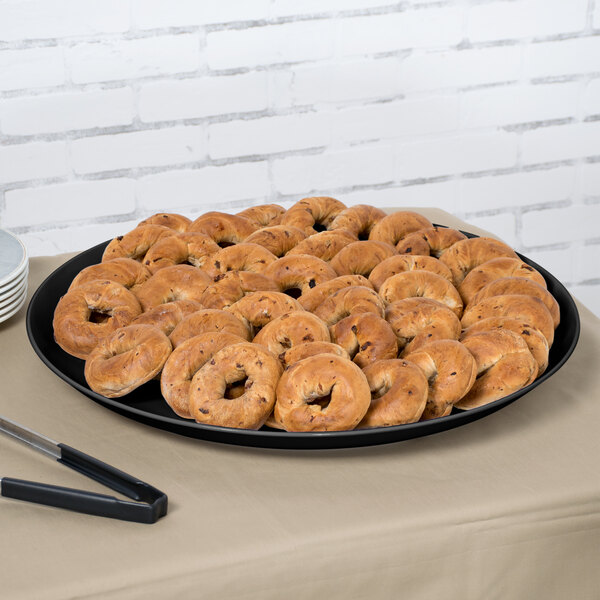A black Siciliano display platter with a tray of bagels on a table.
