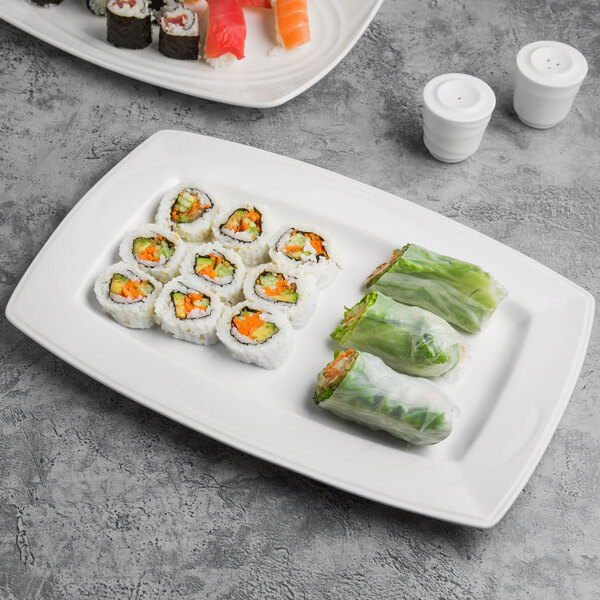 A rectangular white porcelain plate with sushi and rolls on it.