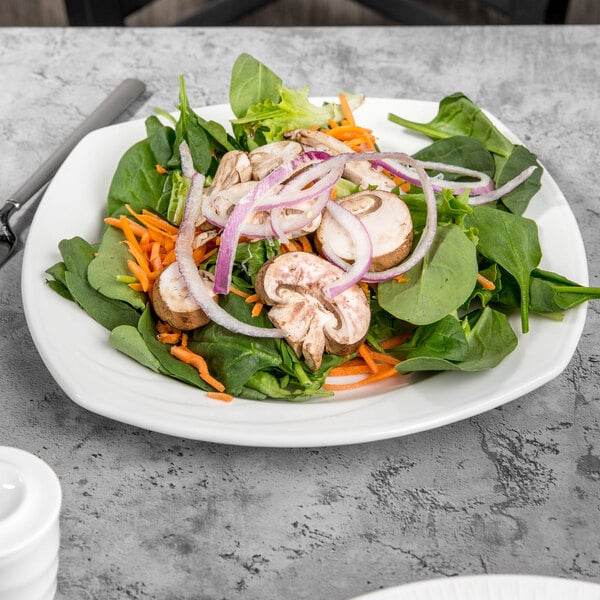 A white Libbey square porcelain plate with salad including spinach, onions, and carrots.