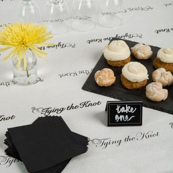 A table with a 40" x 100' Paper Table Cover with a wedding pattern and a plate of cupcakes with white frosting on it.