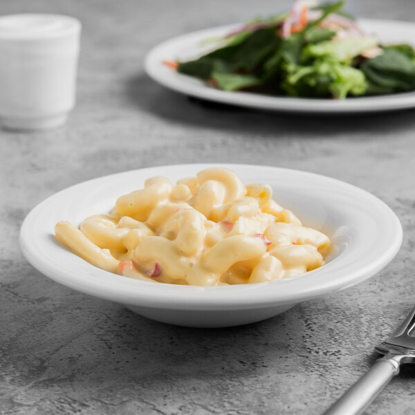A Libbey white porcelain fruit bowl filled with macaroni and cheese next to a plate of salad.