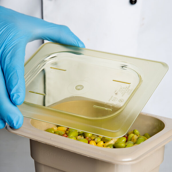 A gloved hand using a Cambro plastic lid to cover a container of food.