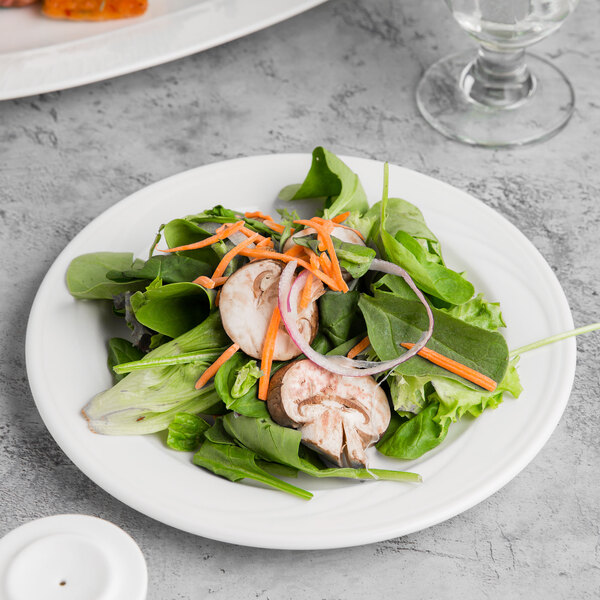 A white Libbey porcelain plate with a salad of spinach, mushrooms, carrots, and onions.
