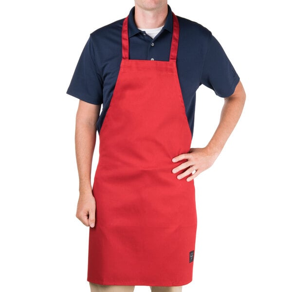 A man wearing a red Chef Revival bib apron standing in a professional kitchen.