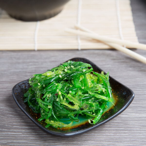 A Libbey square stoneware dip dish with green seaweed on a table.