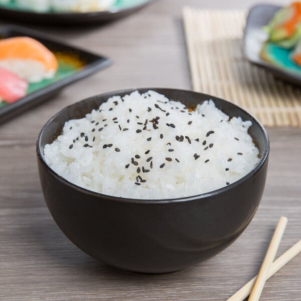 A Libbey stoneware bowl filled with rice topped with black sesame seeds on a table with chopsticks.