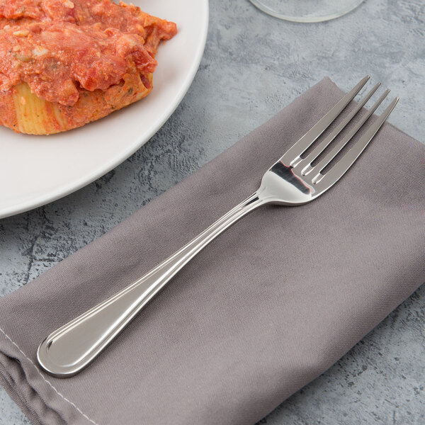 A Bon Chef Tuscany dinner fork on a napkin next to a plate of pasta with red sauce.