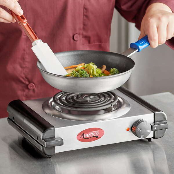 A person cooking vegetables in a pan on an Avantco countertop burner.