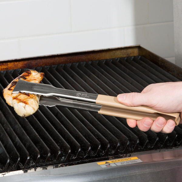 A person using Vollrath Jacob's Pride tongs to turn meat on a grill.