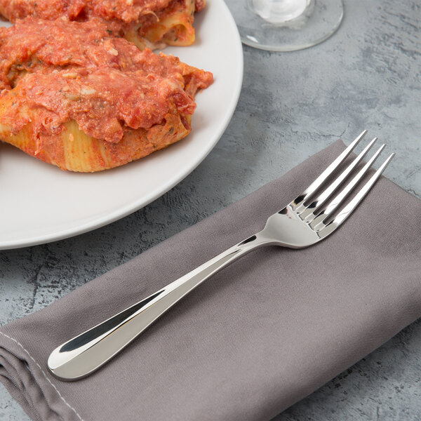 A Bon Chef dinner fork on a napkin next to a plate of pasta with red sauce.