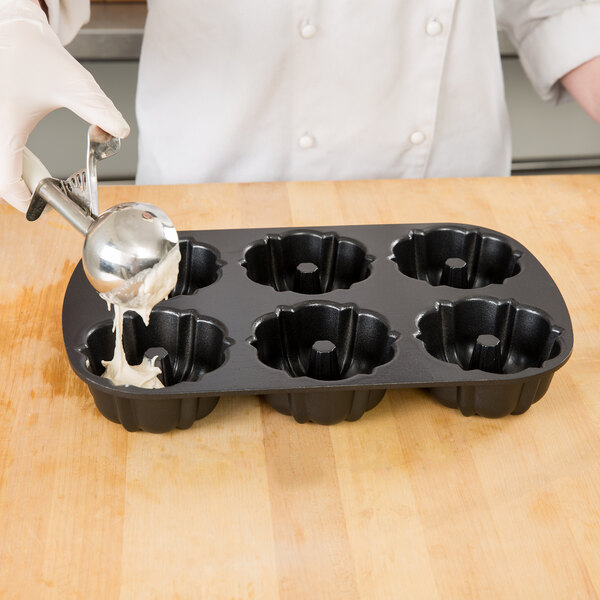 A person pouring batter into a Chicago Metallic mini cake pan with 6 holes.