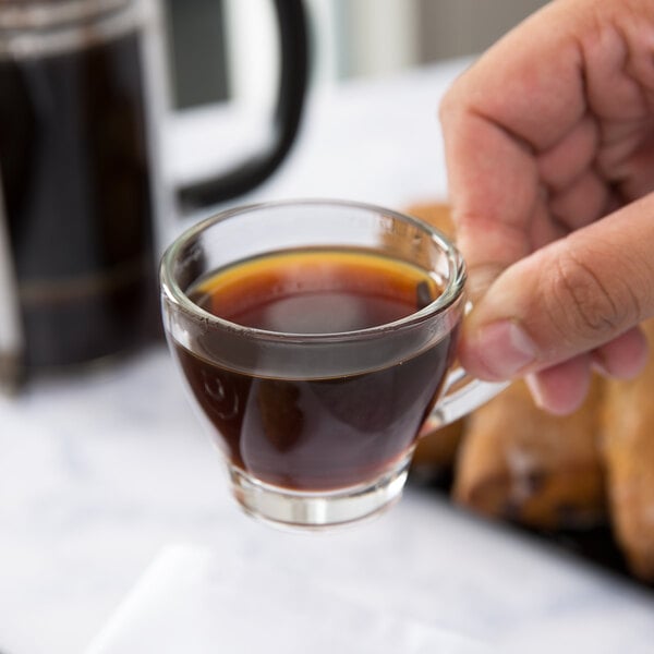 A hand holding a Libbey espresso cup filled with coffee.