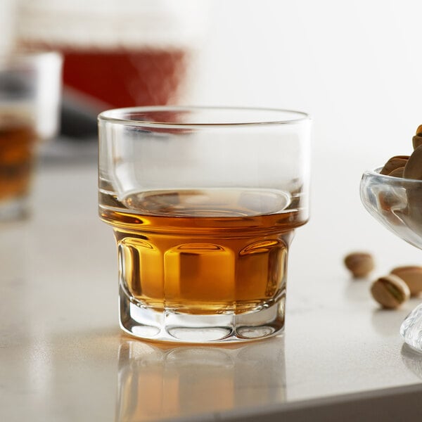 A Libbey Gibraltar rocks glass filled with brown liquid on a table next to a bowl of nuts.