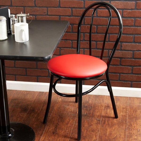 A Lancaster Table & Seating hairpin chair with a red vinyl seat next to a black table in a restaurant.