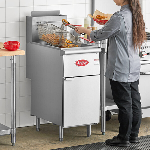 A woman using an Avantco liquid propane floor fryer to cook food in a commercial kitchen.