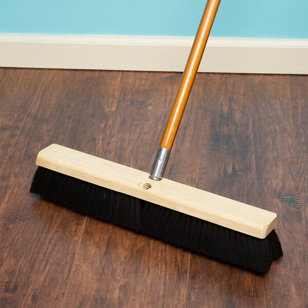 A Carlisle Tampico broom head with a wood handle on a wood floor.