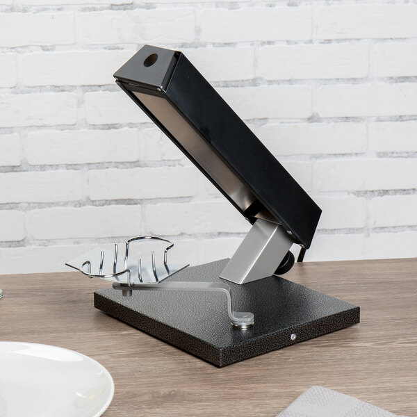 A black and silver Bron Coucke round cheese raclette machine on a table next to a white plate.