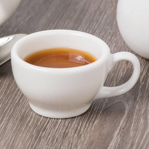 A Libbey ivory porcelain coffee cup filled with brown liquid on a table.